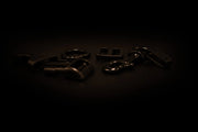 Verschiedene schwarze Metall- und Kunststoffbeschläge wie Schnallen, Karabiner und Verbindungselemente auf einer dunklen Oberfläche angeordnet
