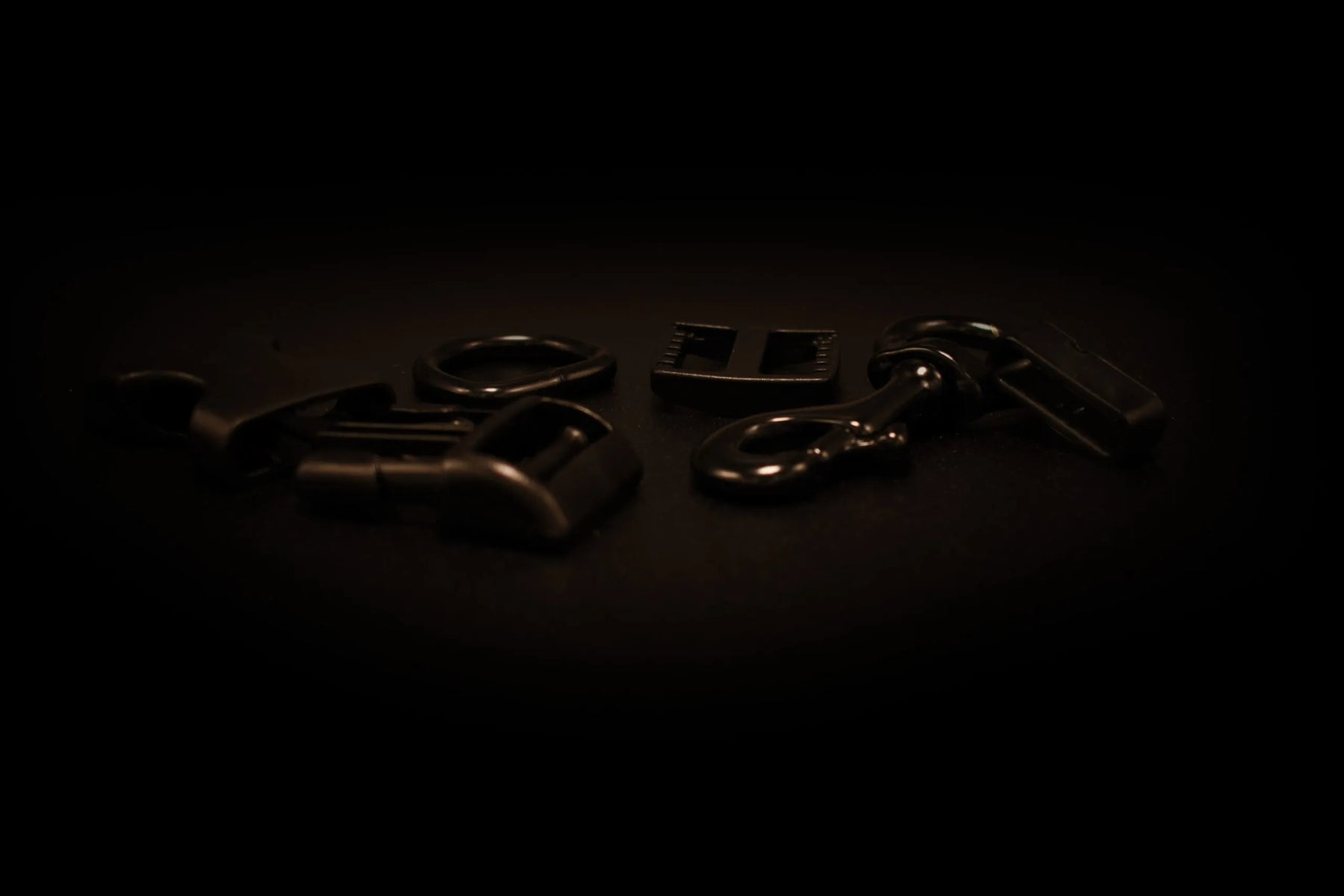 Verschiedene schwarze Metall- und Kunststoffbeschläge wie Schnallen, Karabiner und Verbindungselemente auf einer dunklen Oberfläche angeordnet