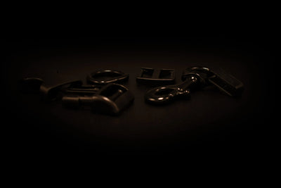 Verschiedene schwarze Metall- und Kunststoffbeschläge wie Schnallen, Karabiner und Verbindungselemente auf einer dunklen Oberfläche angeordnet