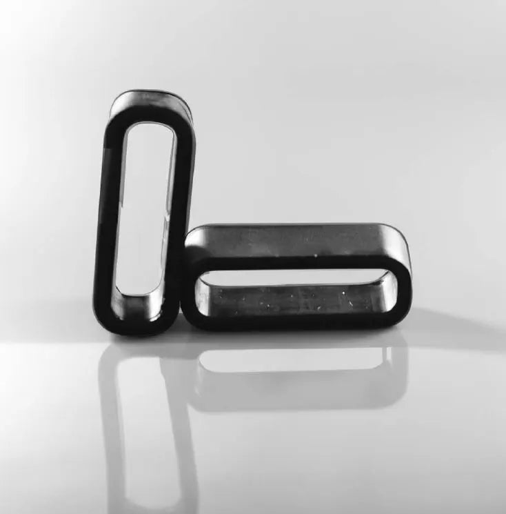 Zwei schwarze rechteckige Schlaufen mit abgerundeten Kanten auf einer glänzenden reflektierenden Oberfläche, eine aufrecht stehend und eine horizontal liegend