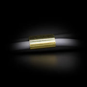 Nahaufnahme eines weißen Seils, das durch eine kleine zylindrische Metallhülse mit glänzender goldfarbener Oberfläche geführt ist, vor dunklem Hintergrund