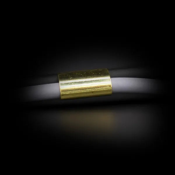 Nahaufnahme eines weißen Seils, das durch eine kleine zylindrische Metallhülse mit glänzender goldfarbener Oberfläche geführt ist, vor dunklem Hintergrund