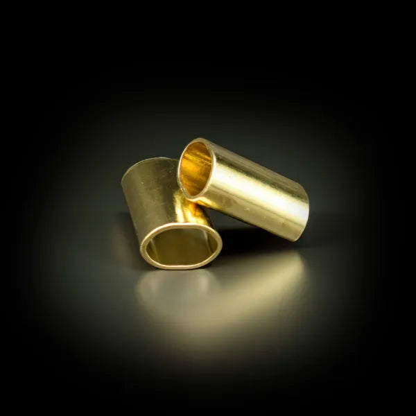 Zwei zylindrische Metallhülsen mit glänzender goldfarbener Oberfläche schräg auf einer dunklen reflektierenden Fläche positioniert