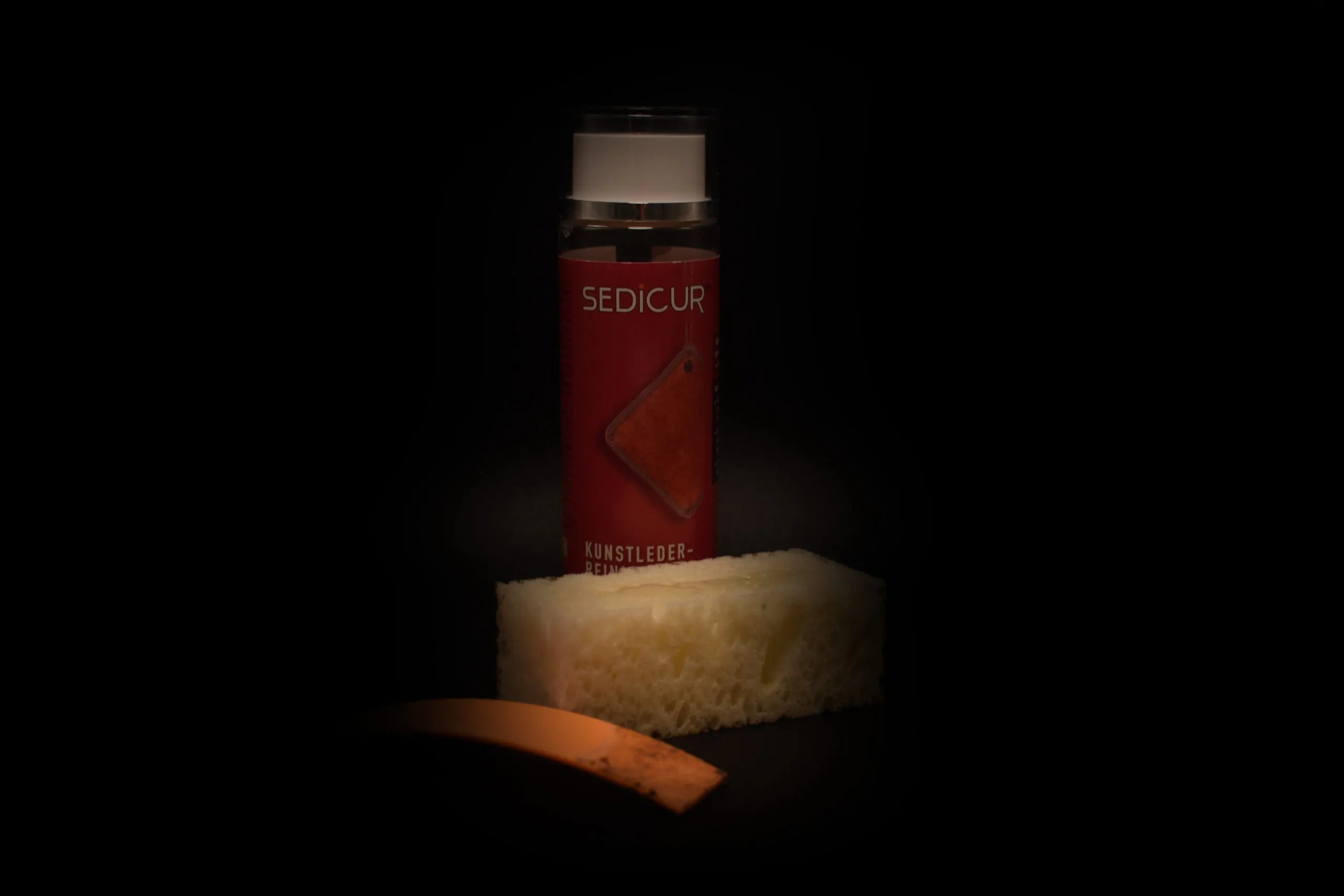 Sedicur Kunstleder-Reiniger Flasche mit Schwamm und Lederprobe, in Nahaufnahme vor dunklem Hintergrund